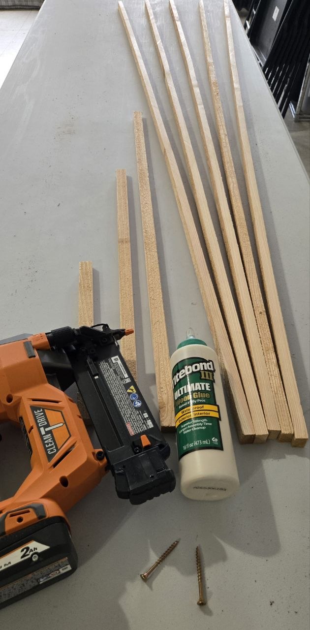 Cedar fence picket ripped into 7/8 inch strips with shorter 1, 2, and 3 foot spreader pieces laid out beside glue, screws, and a pin nailer