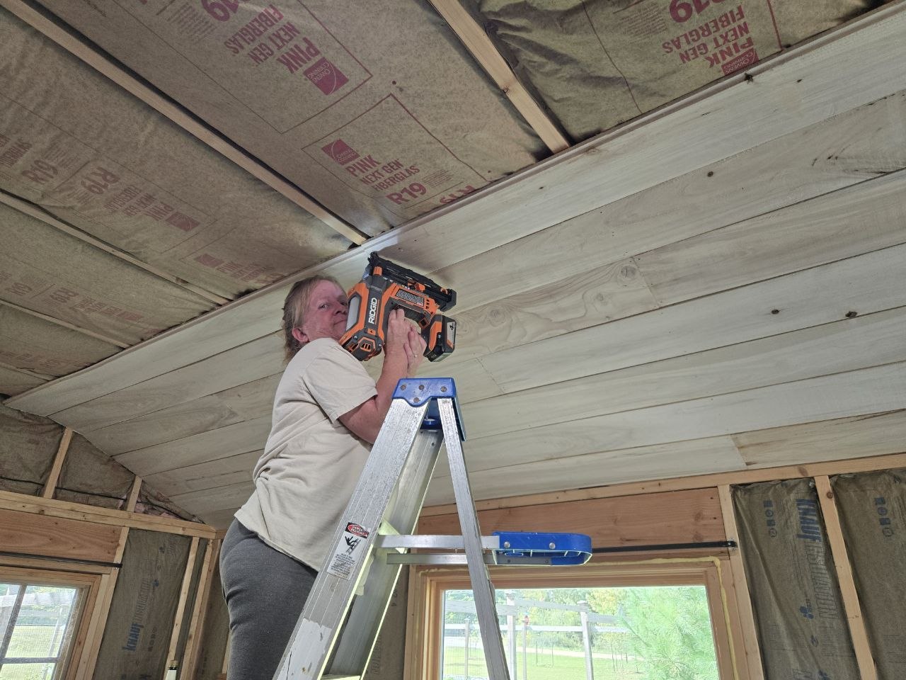 Vanessa on a ladder helping install the homemade shiplap ceiling in the cabin