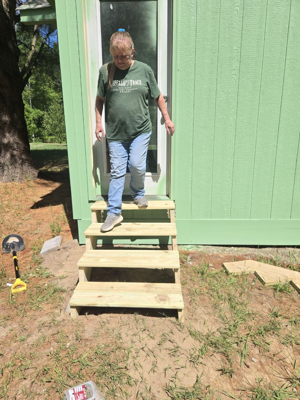Finished wooden steps leading up to the green storage shed at the cabin in June 2026